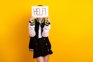 Young female student holding a sign with the word help against a yellow background, emphasizing...