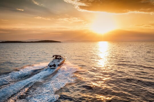 Rear view of a sports motor boat cruising with high speed into the colorful sunset - Powered by Adobe