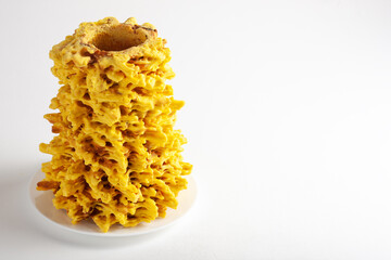 Golden brown Sakotis, a traditional Lithuanian tree cake, displayed upright on a white plate with a minimalist white background. Top view, copy spase