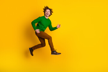 Joyful young man jumps energetically wearing casual outfit against a vibrant yellow wall showcasing...