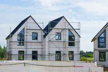 Modern two-story house under construction with scaffolding and unfinished exterior walls