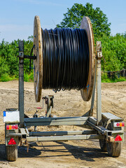 Large cable drum on trailer with black utility cable at construction site under clear sky