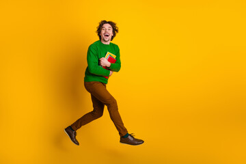 Energetic young man jumping with colorful book against yellow background conveying enthusiasm and...