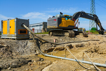 Construction site with dewatering pump, pipes, and excavator during groundwater removal process