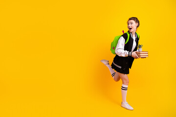 Excited teenage girl in trendy outfit holding book and plant posing on bright yellow background for...