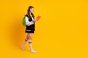 Young student in sporty attire holding a book while walking against vibrant yellow backdrop,...
