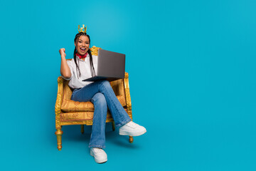 Young woman enjoying a successful moment with her laptop seated on a luxurious chair against a...