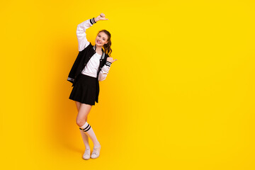 Charming young female student in casual attire poses against a vibrant yellow wall, exuding...