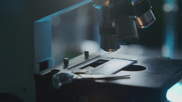 Close up view of glass slide with specimen on stage being moved under microscope objective lens during laboratory examination