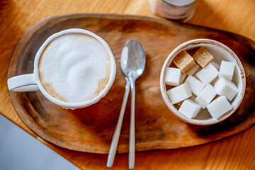 Cappuccino cup with a spoon and diced sugar on a wooden breakfast tray