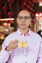 Bald Hispanic man wearing pink casual business shirt and eyeglasses in Chinese style tea house