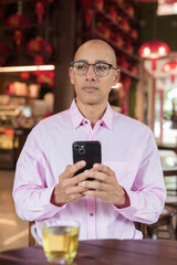 Bald Hispanic man wearing pink casual business shirt and eyeglasses in Chinese style tea house