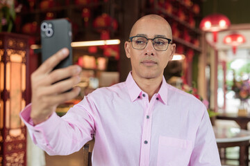 Bald Hispanic man wearing pink casual business shirt and eyeglasses in Chinese style tea house