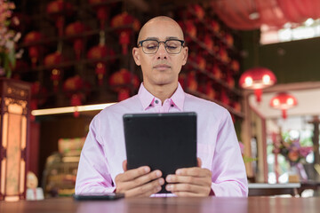 Bald Hispanic man wearing pink casual business shirt and eyeglasses in Chinese style tea house