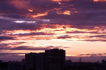 Dramatic sunrise illuminates the city skyline with colorful, textured clouds above silhouette buildings. Concept of: Urban dawn.
