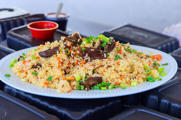 Flavorful beef fried rice topped with green onions served on white plate in an outdoor setting