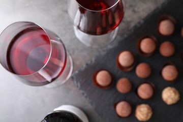 Red wine in glasses and tasty truffle bonbons on grey table, flat lay