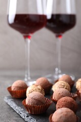 Tasty truffle bonbons and red wine on grey textured table, closeup