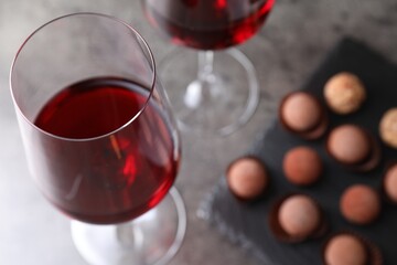 Red wine in glasses and tasty truffle bonbons on grey table, selective focus