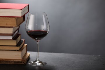 Red wine in glass and stack of books on grey textured table, closeup. Space for text