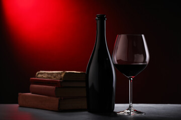 Tasty wine and stacked books on dark table in red light, closeup