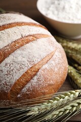 Fresh bread, flour and green wheat spikes on table, closeup