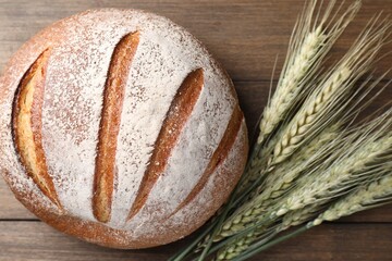 Fresh bread and green wheat spikes on wooden table, flat lay