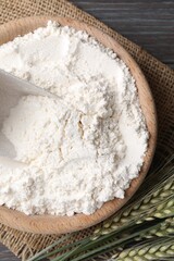 Flour in bowl and green wheat spikes on wooden table, flat lay