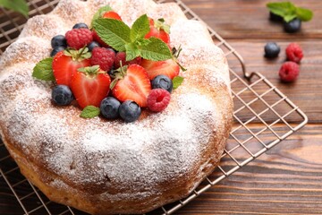 Tasty Bundt cake with powdered sugar and berries on wooden table, closeup