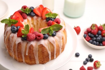 Delicious bundt cake with berries, glaze and mint on white table, closeup