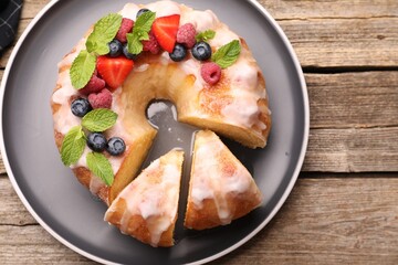 Pieces of delicious bundt cake with berries, glaze and mint on wooden table, top view