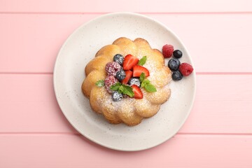 Delicious bundt cake with powdered sugar, berries and mint on pink wooden table, top view