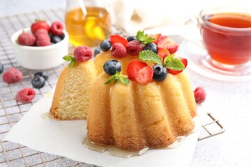 Tasty Bundt cake with berries, honey, mint and tea on light grey table, closeup