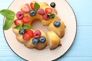Tasty Bundt cake with berries and mint on light blue wooden table, top view