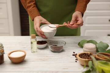 Making natural scrub. Woman adding sugar into bowl at white wooden table, closeup