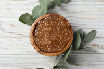 Natural body scrub in bowl and eucalyptus branches on wooden table, flat lay