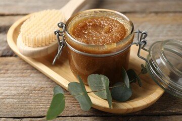 Natural body scrub in glass jar, brush and eucalyptus branch on wooden table, closeup