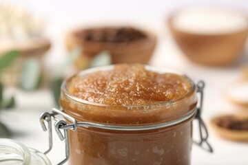 Natural body scrub in glass jar on blurred background, closeup