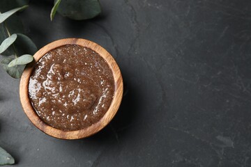 Natural body scrub and eucalyptus leaves on black table, flat lay. Space for text