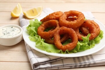 Fried squid rings, lemon, lettuce and sauce on light wooden table, closeup
