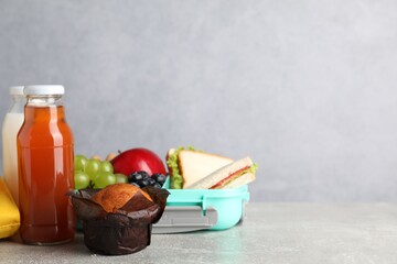 Open lunch box with delicious food, juice and milk on grey table, closeup. Space for text
