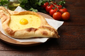 Tasty khachapuri with cheese, egg, tomatoes and parsley on wooden table, closeup. Space for text