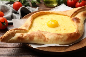Tasty khachapuri with cheese, egg, tomatoes and parsley on wooden table, closeup