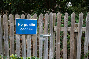 Fototapeta premium No Public Access sign on a locked wooden gate and fence, with trees and bushes behind. Restricted entry, private property concept in rural setting.