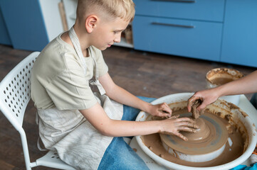 Boy sculpting clay on pottery wheel, children's activity with teacher