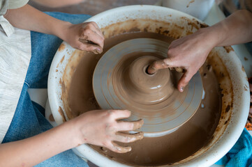 Hands of child and adult shaping clay together on pottery wheel
