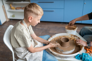 Child and instructor shaping clay together at pottery workshop