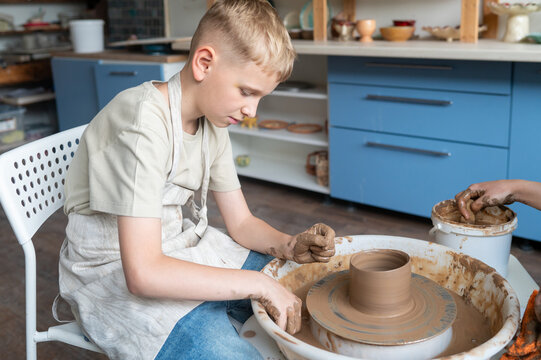 Boy sculpting clay on pottery wheel, children's activity with teacher - Powered by Adobe