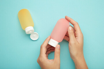 Hand holding plastic tube for travel on blue background. Cosmetic beauty product branding mockup.