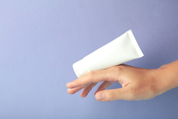 Hand holding blank white plastic tube on purple background. Cosmetic beauty product branding...